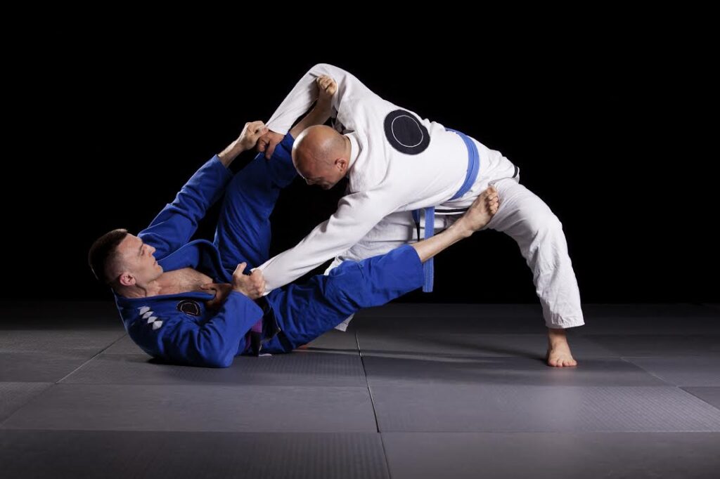 Two adult students in gi demonstrating a guard position on the mat