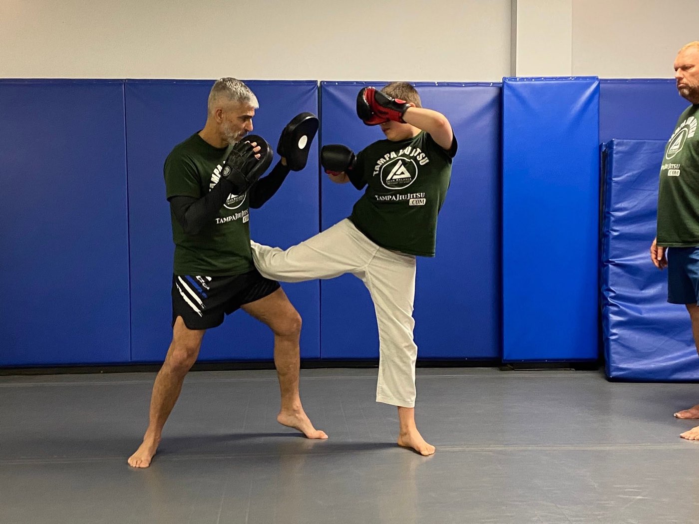 An adult student throwing a kick into the coach’s pads during Muay Thai class