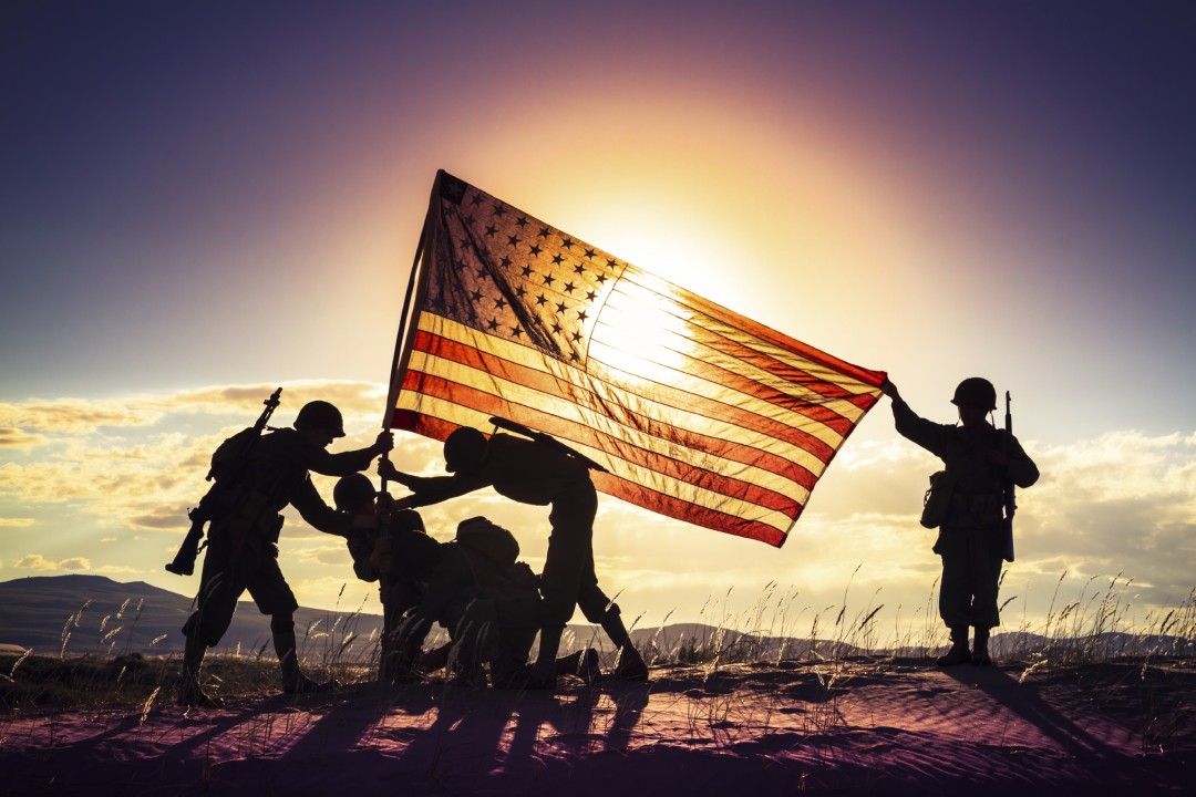 Silhouetted service members raising the American flag at sunset